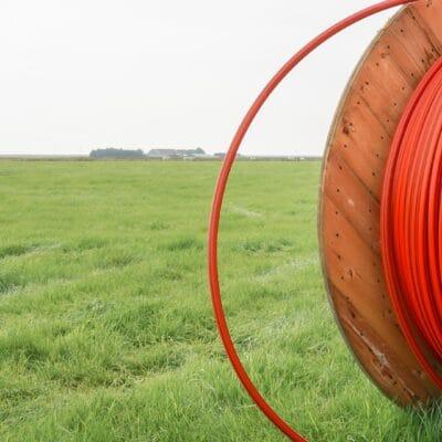 A large spool of orange fiber optic broadband cable sits in an expansive grassy field in a rural setting.