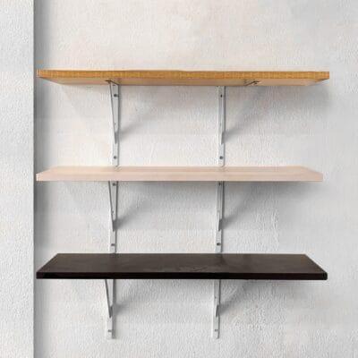 Three floating shelves are attached to a large white wall. Each shelf has a different shade of brown.
