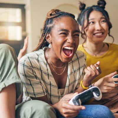 Three people sitting on a couch together and playing a video game on an unseen screen. All hold controllers.