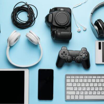 A collection of devices, including a gaming controller, headphones, a tablet, and a phone, arranged on a blue surface.
