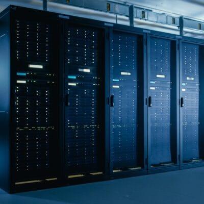A dimly lit data center aisle with rows of server racks on both sides, glowing with green and blue lights from active servers.