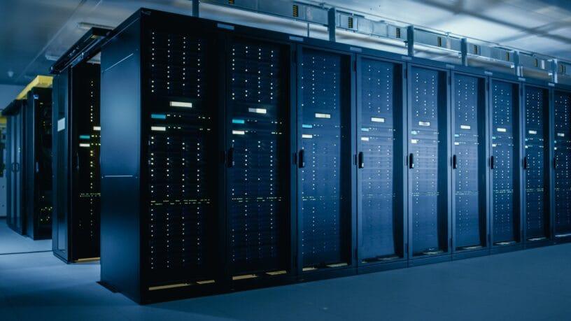 A dimly lit data center aisle with rows of server racks on both sides, glowing with green and blue lights from active servers.