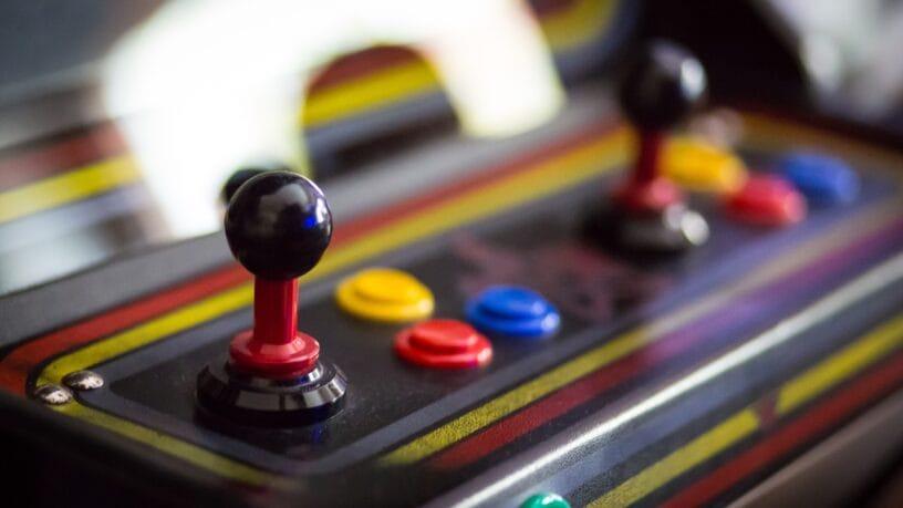 An arcade cabinet with two joy sticks and several buttons. The buttons are different colors.