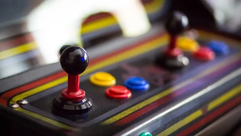 An arcade cabinet with two joy sticks and several buttons. The buttons are different colors.