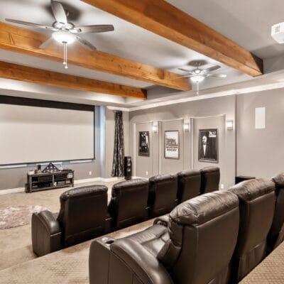 A home theater with two rows of recliners, a large screen, gray walls, and a ceiling decorated with wood beams and fans.