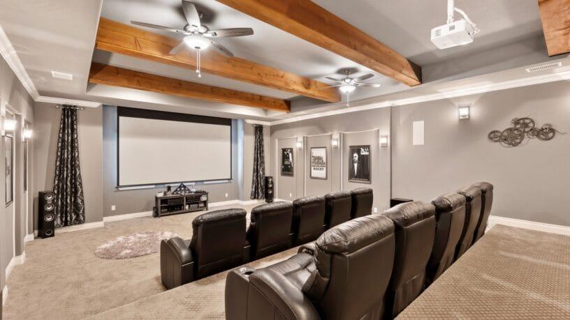 A home theater with two rows of recliners, a large screen, gray walls, and a ceiling decorated with wood beams and fans.