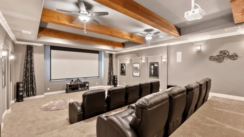 A home theater with two rows of recliners, a large screen, gray walls, and a ceiling decorated with wood beams and fans.