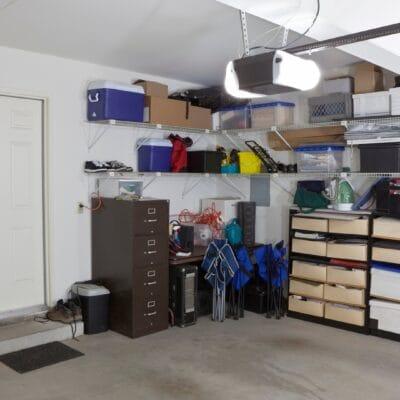 A home garage with white walls and multiple boxes, containers, and tools placed on the right side against the wall.